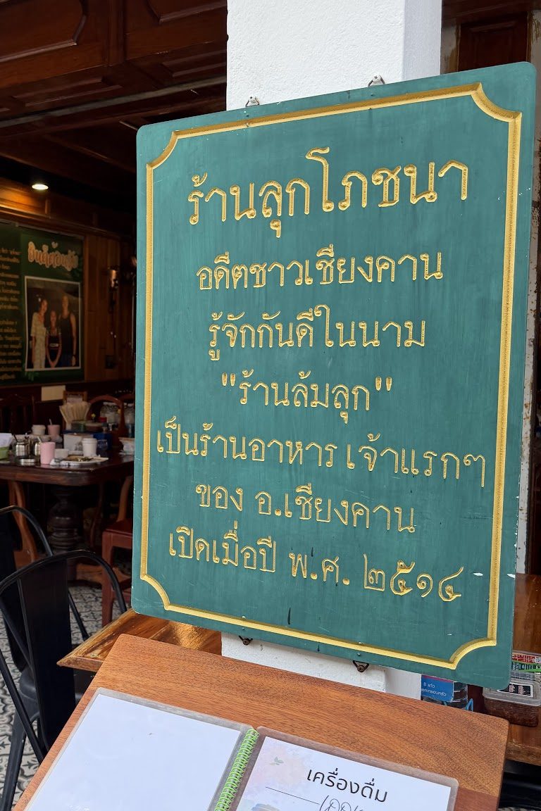 ป้ายประวัติร้านสีเขียว เขียนว่าร้านลุกโภชนา อดีตชาวเชียงคานรู้จักกันดีในนามร้านล้มลุก เป็นร้านอาหารเจ้าแรก ๆ ของ อ.เชียงคาน เปิดเมื่อปี พ.ศ. 2514